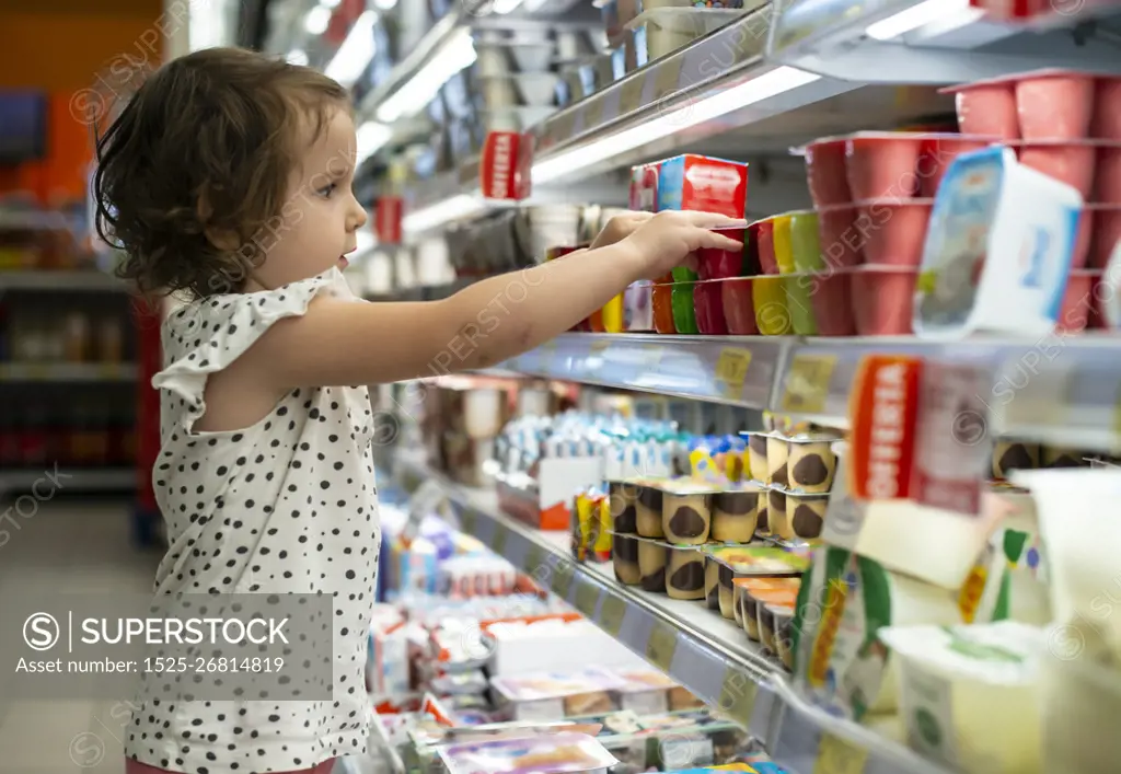 Little girl buying yogurt in supermarket. Child in supermarket select products from store showcase. Concept for children selecting milk products in shop.