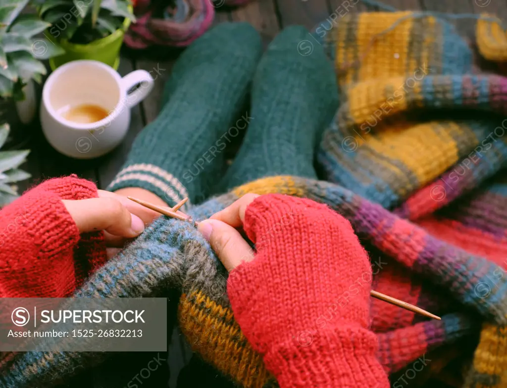 Top view woman feet with socks, sitting at home balcony, hand with knitted gloves hold knitting needle to knit colorful wool scarf  for meaningful handmade winter gift when wintertime come.