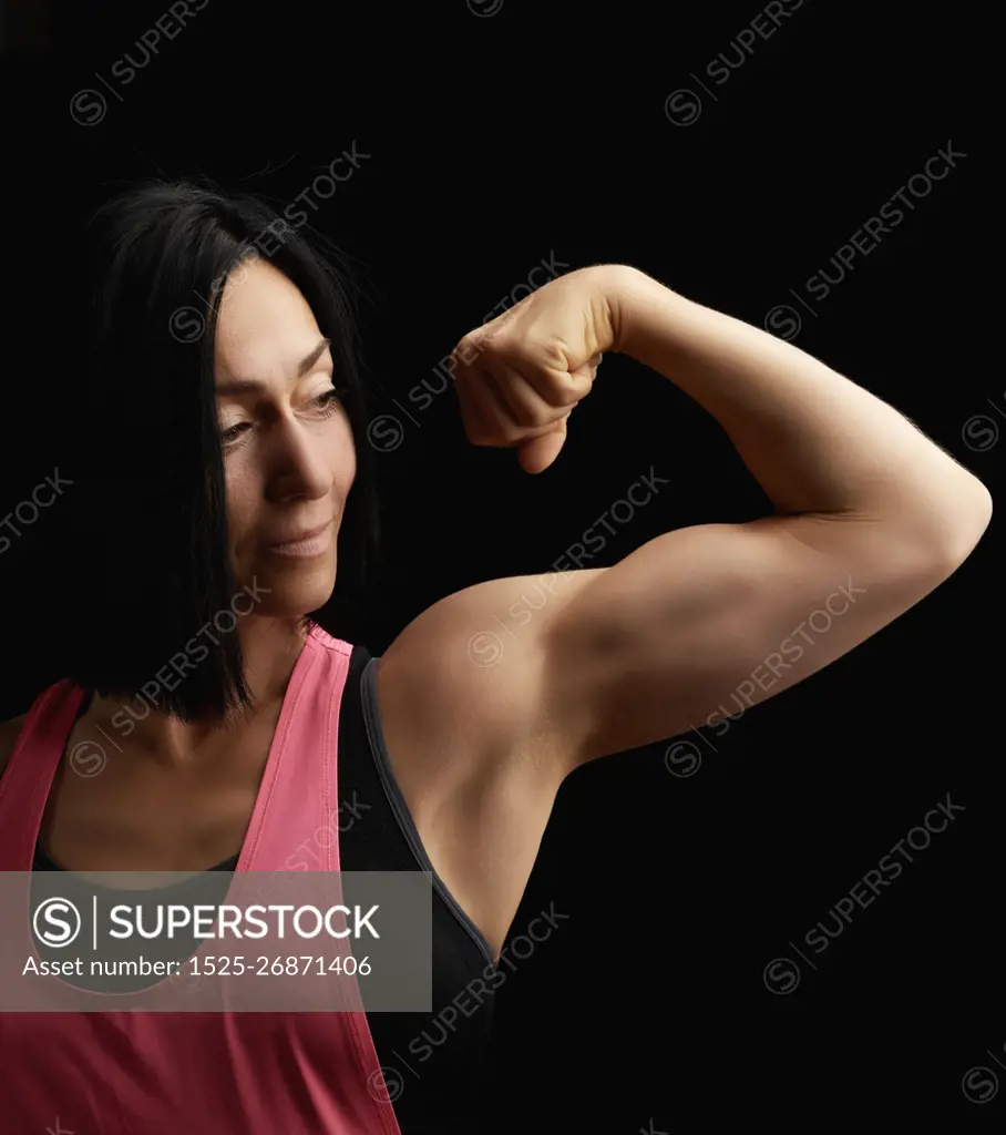 beautiful athletic girl raised and bent her arm demonstrating her biceps, athlete is standing on a dark background, wearing a black top 
