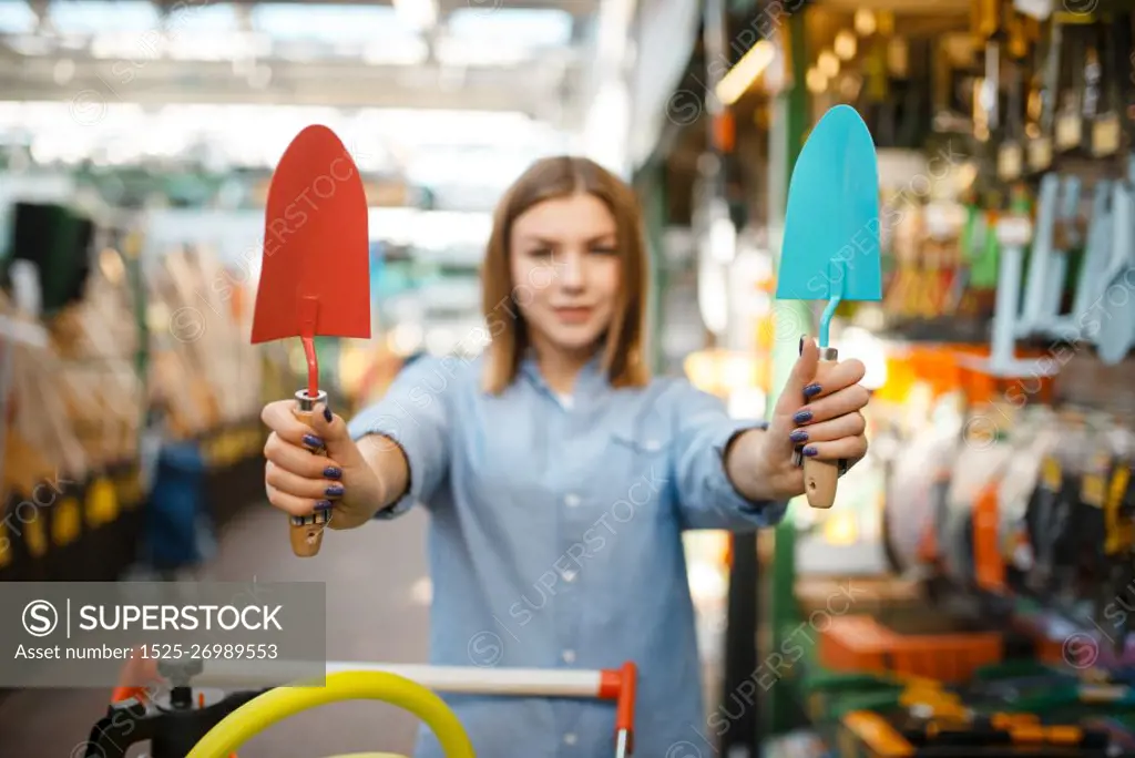 Female customer choosing garden shovel in shop for gardeners. Woman buying equipment in store for floriculture, florist instrument purchasing. Customer choosing garden shovel, gardeners shop