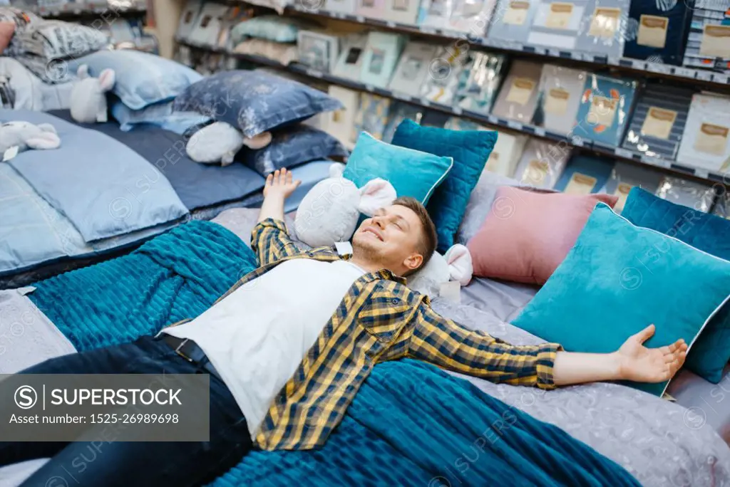 Young man lying on the bed in bedding store. Male person buying home goods in market, guy sleeping in shop. Young man lying on the bed in bedding store