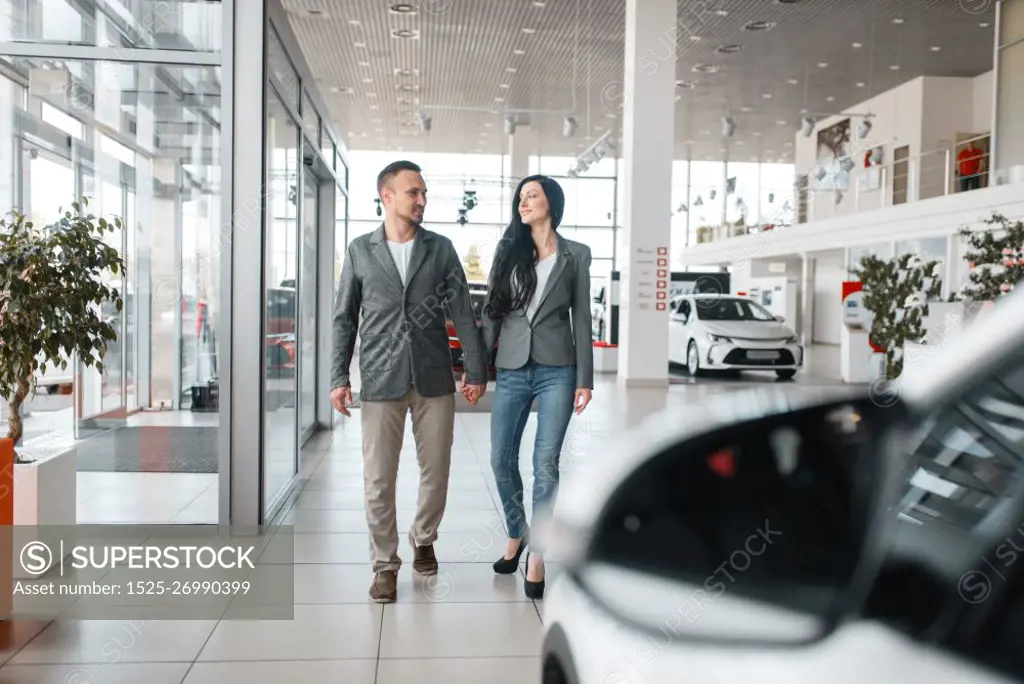 Happy couple buying new car in showroom. Male and female customers choosing vehicle in dealership, automobile sale, auto purchase. Happy couple buying new car in showroom