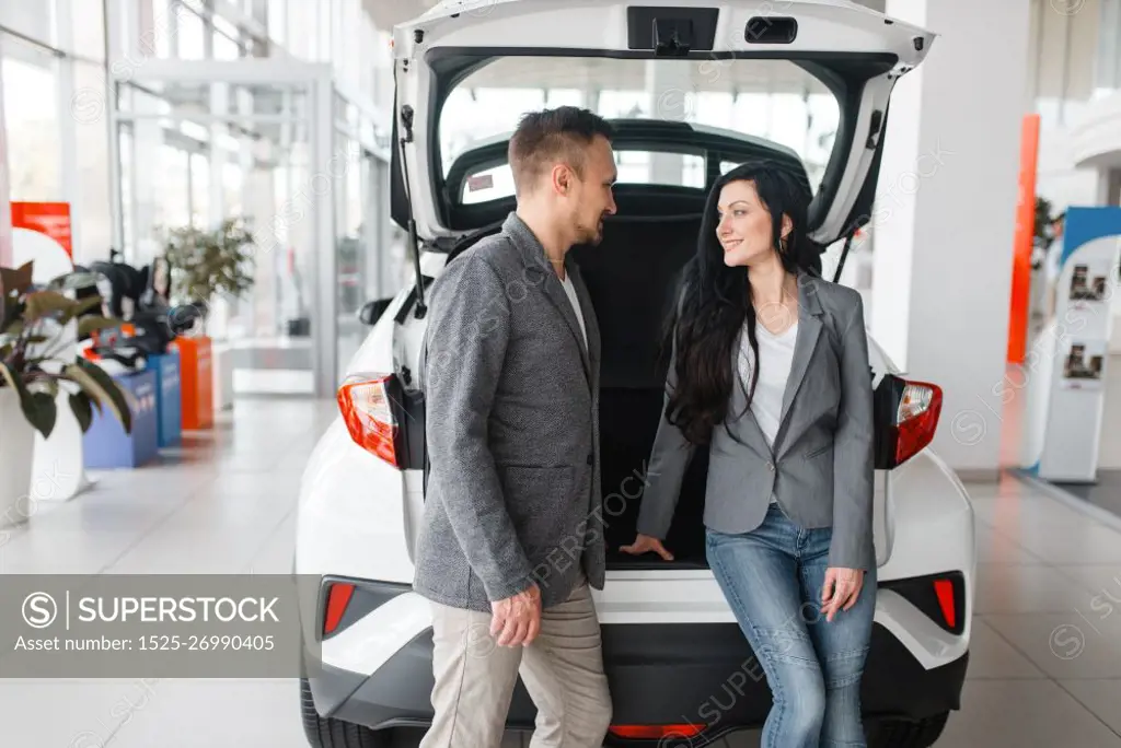 Couple buying new car in showroom, man and woman near the opened trunk. Male and female customers choosing vehicle in dealership, automobile sale, auto purchase