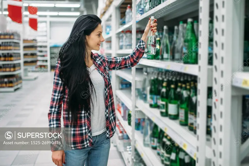 Young woman buying mineral water in supermarket. Female customer on  shopping in hypermarket, department of beverages