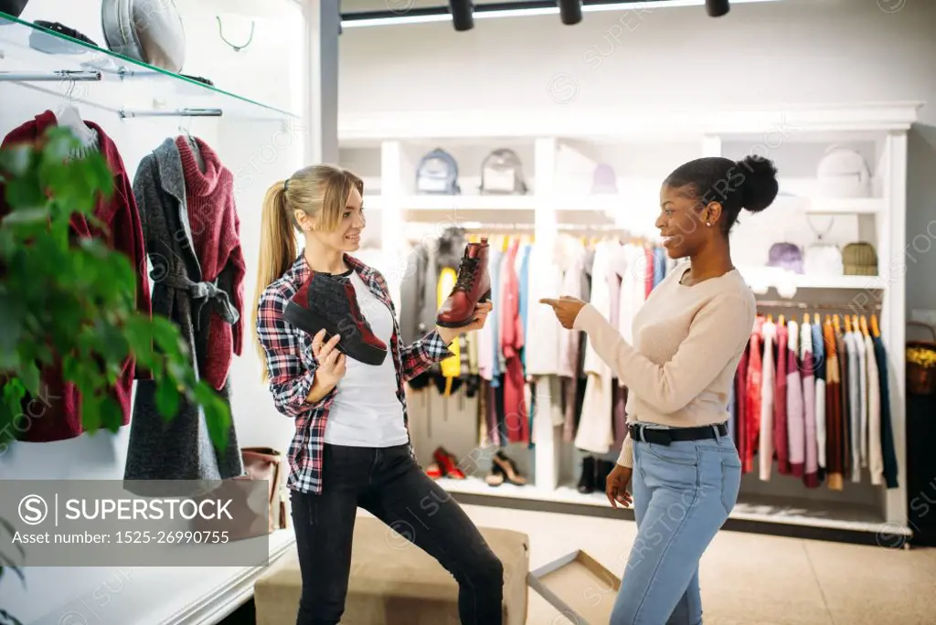 Two females buying clothes and shoes, shopping. Shopaholics in clothing store, consumerism lifestyle, fashion