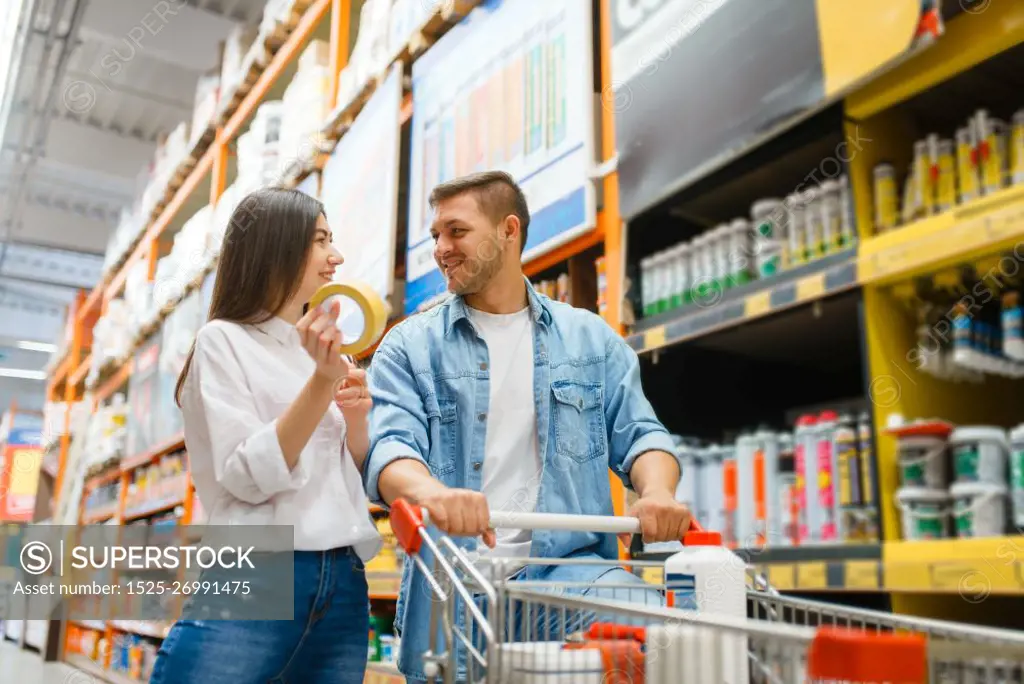 Couple with a cart buying building materials in hardware store. Customers look at the goods in diy shop. Couple with a cart buying building materials