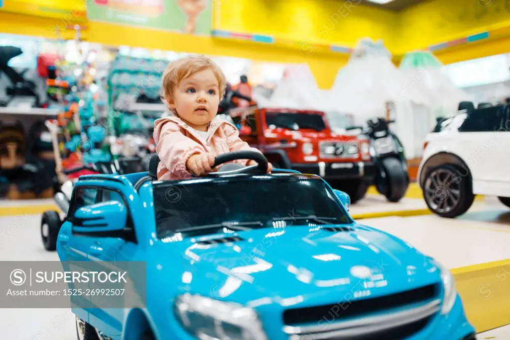 Little girl choosing electromobile in kids store, front view. Daughter buying toys in supermarket, family shopping, young customer