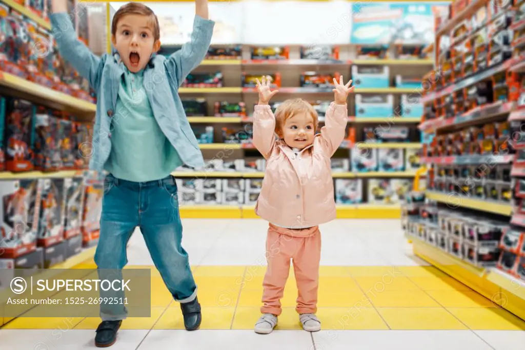 Little boy and girl raised their hands up at the shelf in kids store, happy children. Brother and sister choosing toys in supermarket, family shopping, young customers