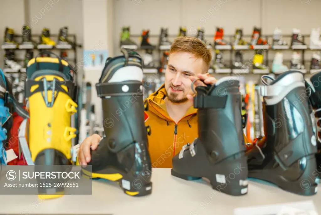 Male person at the showcase choosing ski or snowboarding boots, shopping in sports shop. Winter season extreme lifestyle, active leisure store, customer buying skiing equipment