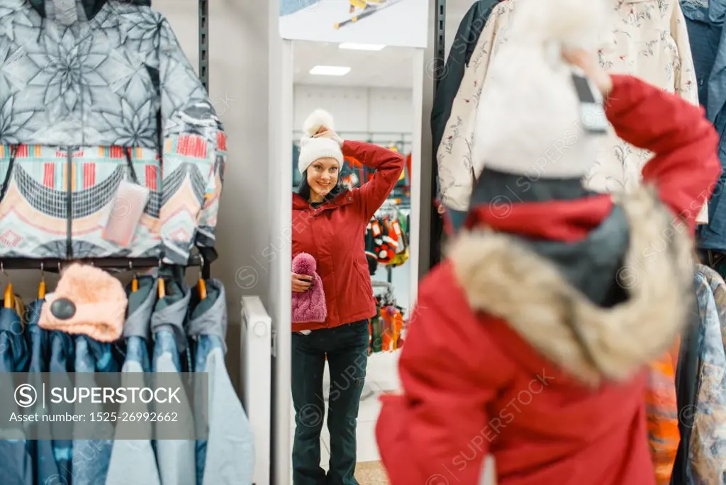 Woman at the showcase choosing skiing or snowboarding equipment, shopping in sports shop. Winter season extreme lifestyle, active leisure store, customer buying ski suit