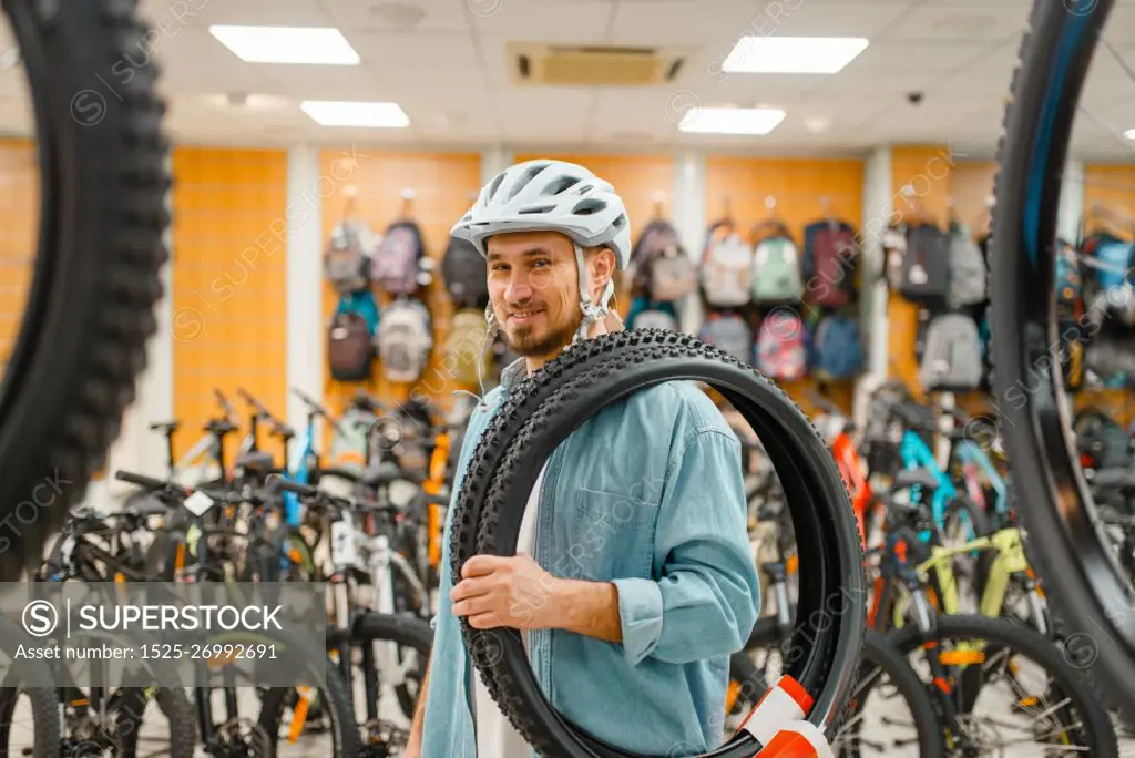 Man in cycling helmet holds bicycle tyres, shopping in sports shop. Summer season extreme lifestyle, active leisure store, customers buying bike equipment. Man in cycling helmet holds bicycle tyre, shopping