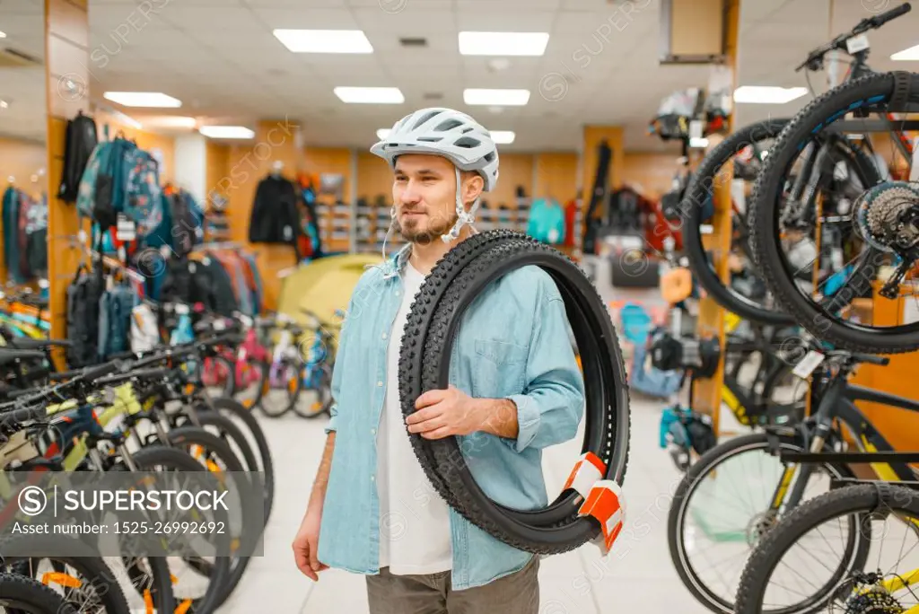 Man in cycling helmet holds bicycle tyres, shopping in sports shop. Summer season extreme lifestyle, active leisure store, customers buying bike equipment