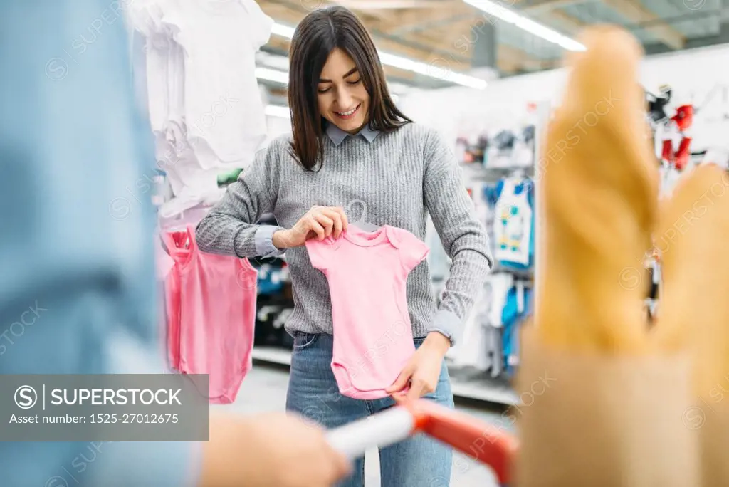 Young mother buying childrens clothes in store, family shopping. Customers in shop, buyers in market, department of goods for kids