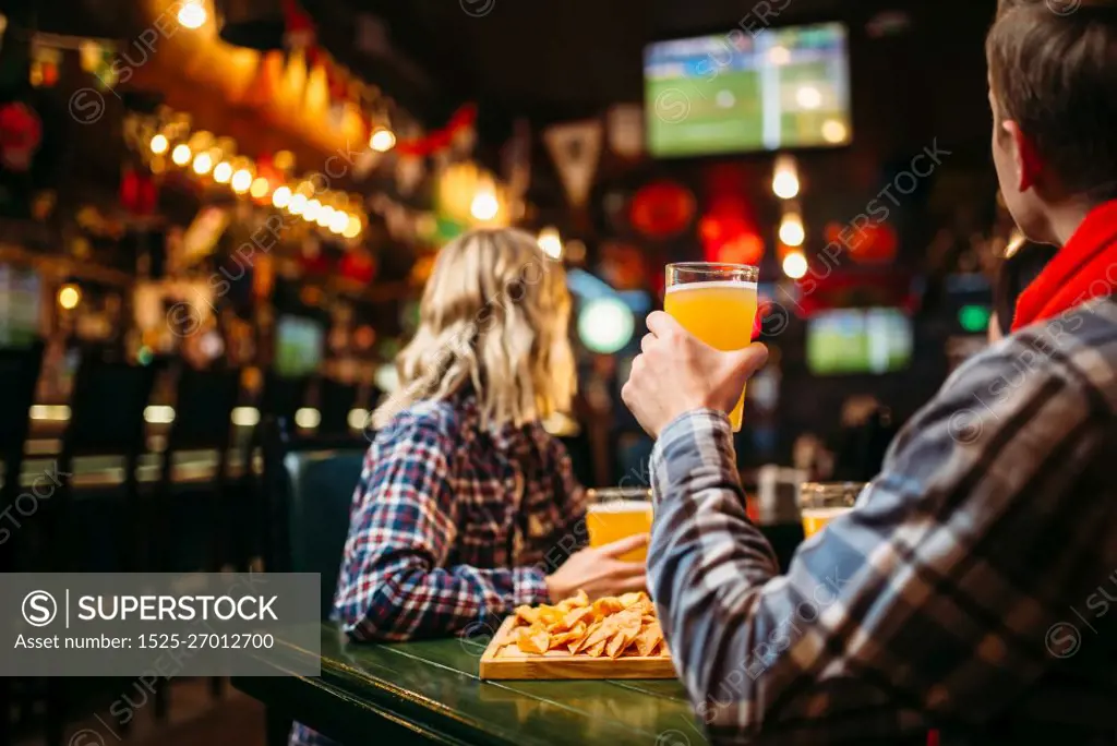 Football fans watching match and drinks beer at the table in sports bar. Tv broadcasting, young friends leisures in the pub. Fans watching match and drinks beer in sports bar