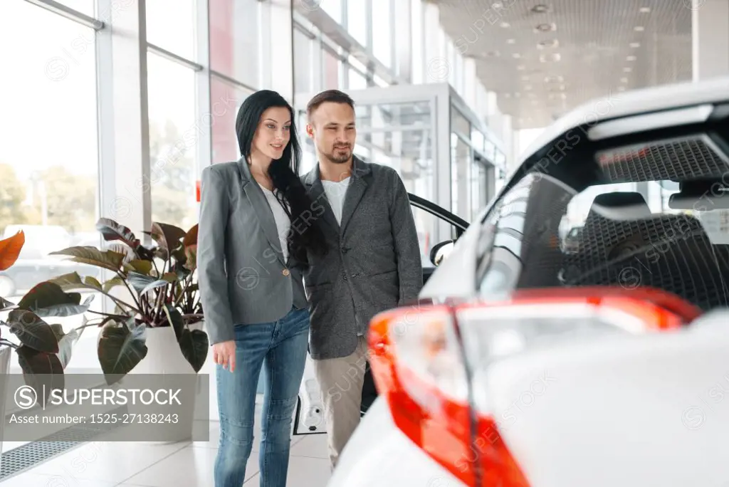 Happy couple buying new car in showroom. Male and female customers choosing vehicle in dealership, automobile sale, auto purchase. Happy couple buying new car in showroom