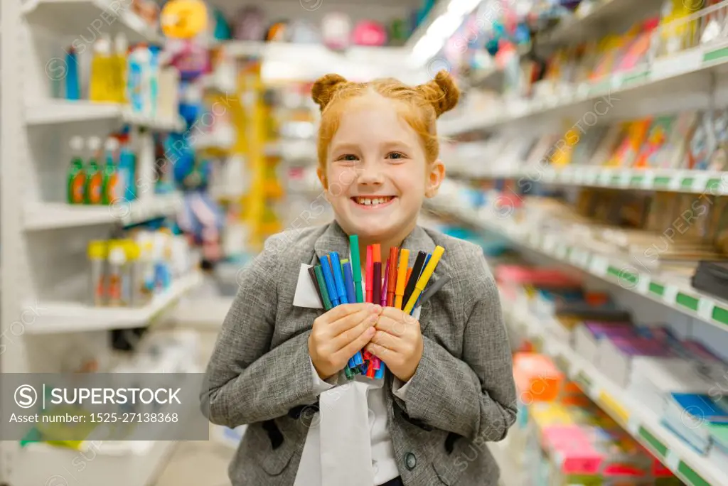 Little school girl holds colorful markers, shopping in stationery store. Female child buying office supplies in shop, schoolchild in supermarket. School girl holds markers, stationery store