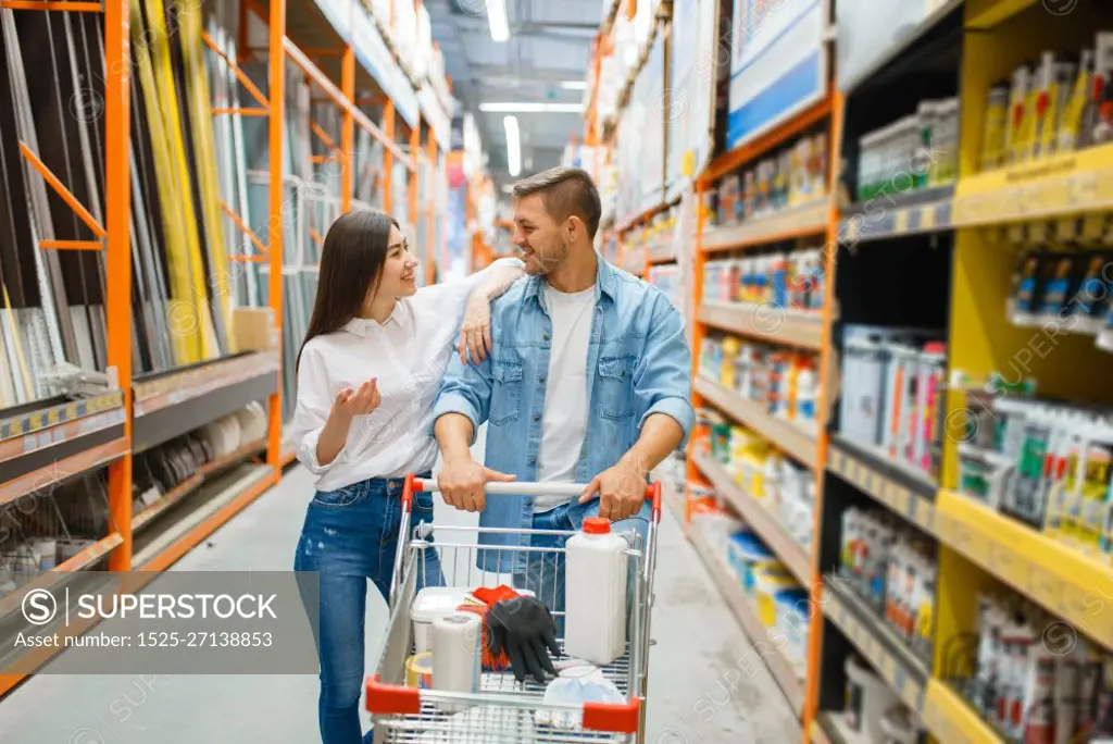 Couple with a cart buying building materials in hardware store. Customers look at the goods in diy shop