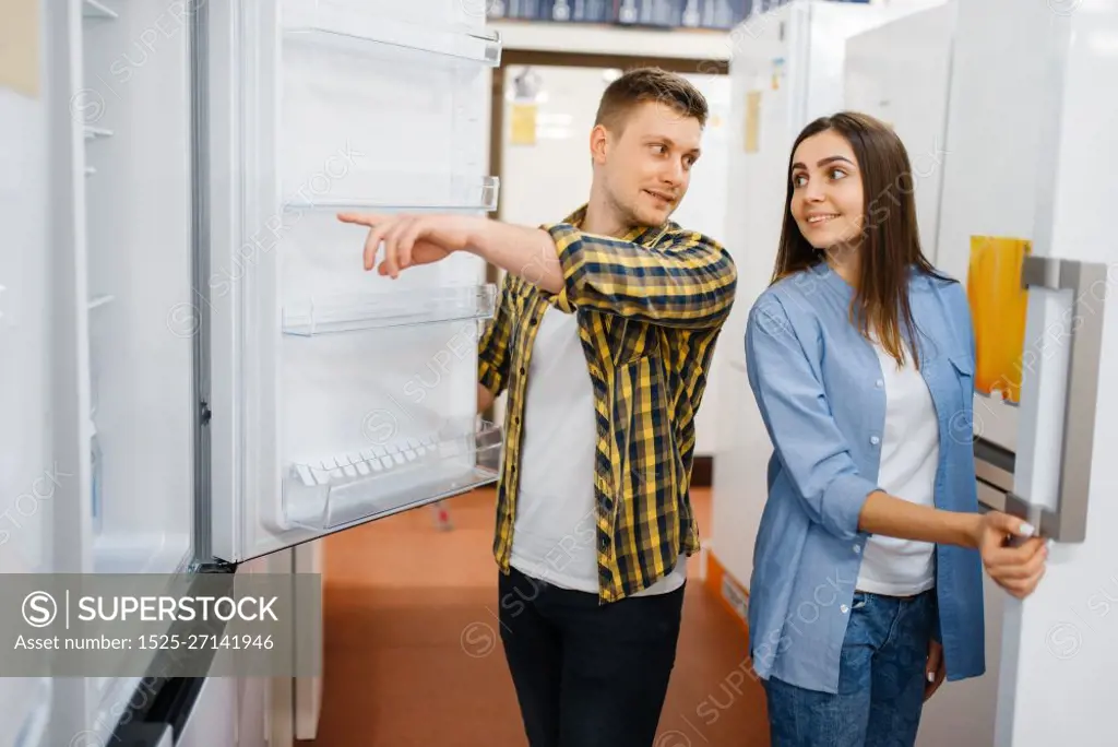 Young family couple choosing refrigerator in electronics store. Man and woman buying home electrical appliances in market. Young couple choosing refrigerator in store