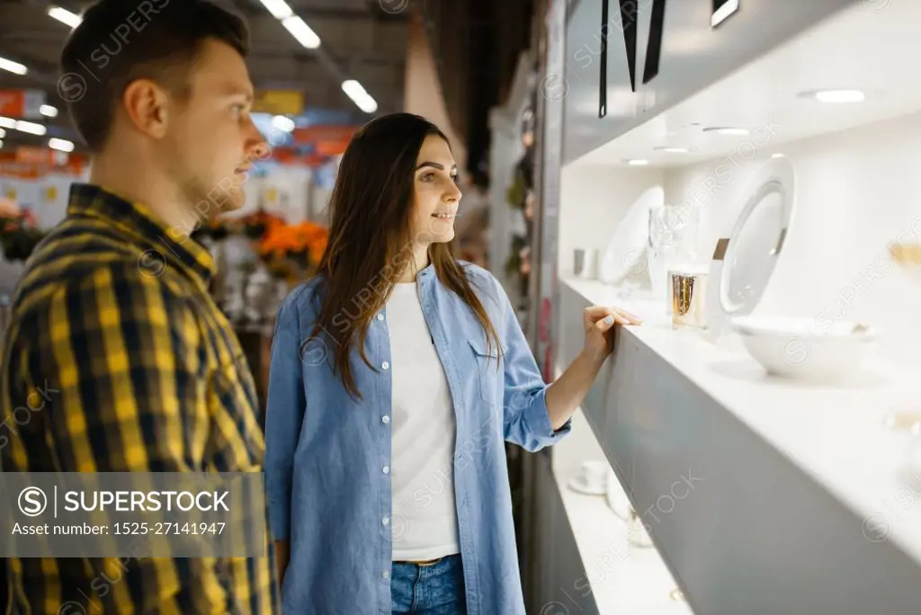 Young couple choosing wineglasses in houseware store. Man and woman buying home goods in market, family in kitchenware supply shop. Couple choosing wine glasses in houseware store