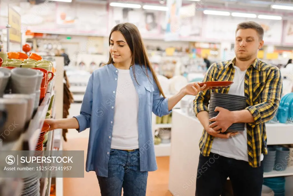 Young couple choosing plates in houseware store. Man and woman buying home goods in market, family in kitchenware supply shop. Young couple choosing plates in houseware store