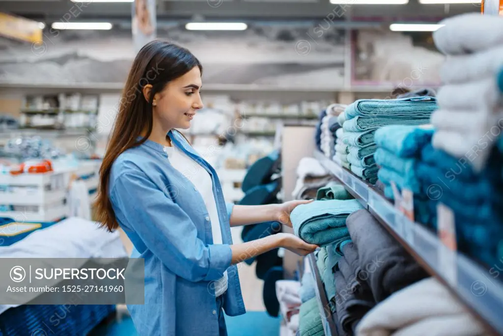 Young woman choosing towel in bed linen store. Female person buying home goods in market, lady in bedding shop. Young woman choosing towel in bed linen store