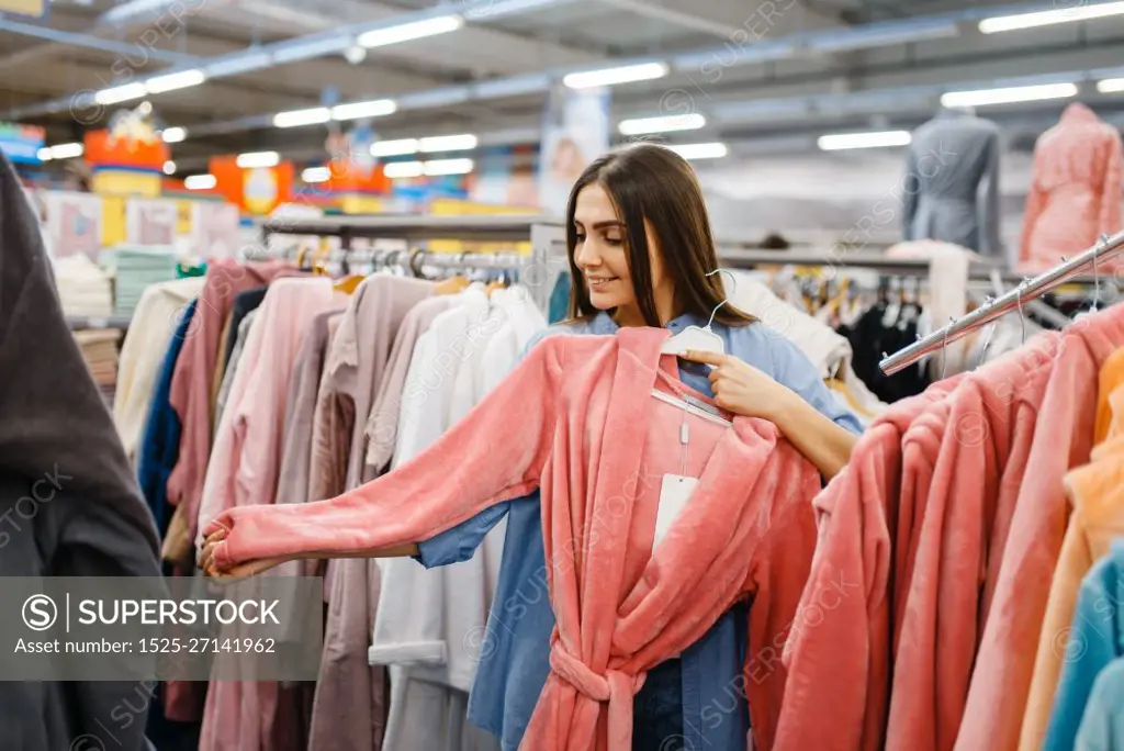 Young woman choosing bathrobe in bed linen store. Female person buying home goods in market, lady in bedding shop. Young woman choosing bathrobe in bed linen store