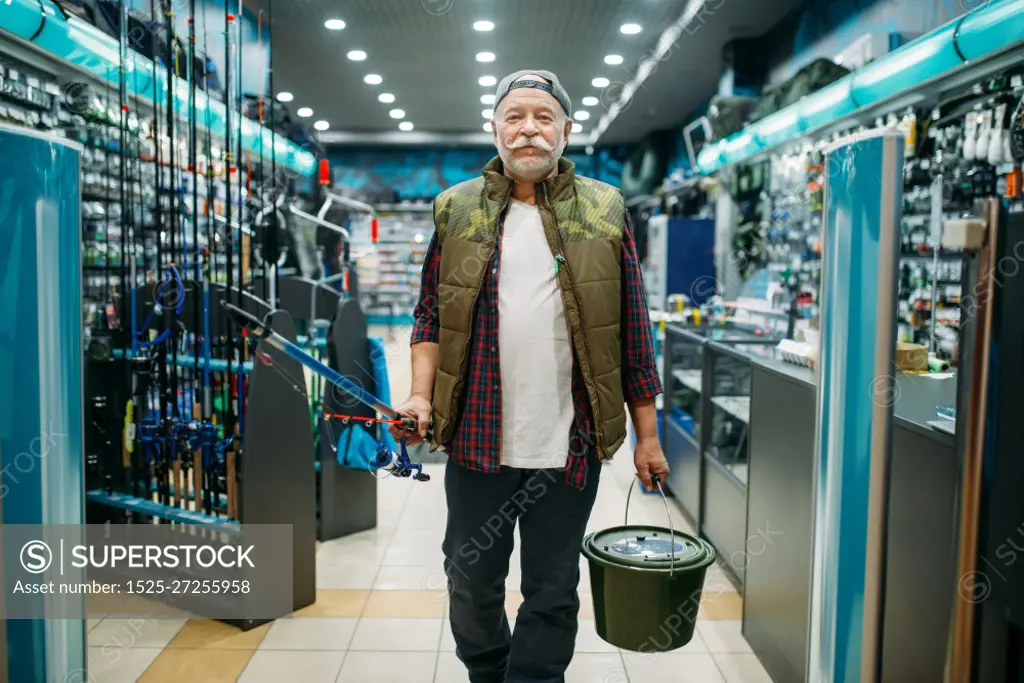 Fisherman with rod and plastic bucket in fishing shop. Male angler buying equipment and tools for fish catching and hunting, assortment on showcase in store. Fisherman with rod and bucket in fishing shop