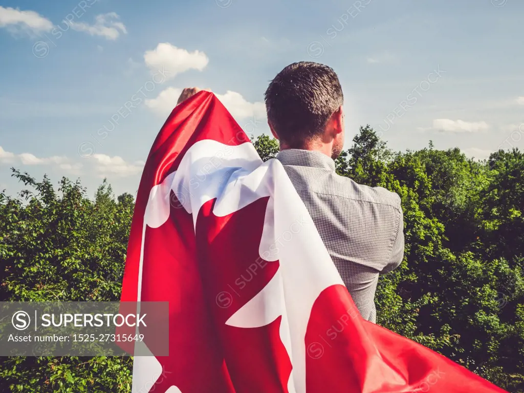 Attractive man holding Canadian Flag on blue sky background on a clear, sunny day. View from the back, close-up. National holiday concept. Attractive man holding Canadian Flag. National holiday