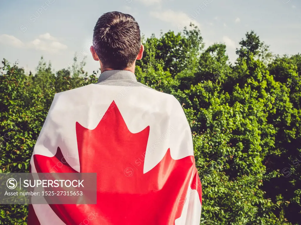 Attractive man holding Canadian Flag on blue sky background on a clear, sunny day. View from the back, close-up. National holiday concept. Attractive man holding Canadian Flag. National holiday