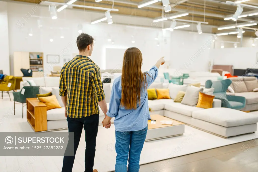 Happy couple choosing furniture in store showroom. Man and woman looking samples for bedroom in shop, husband and wife buys goods for modern home interior. Happy couple choosing furniture in store