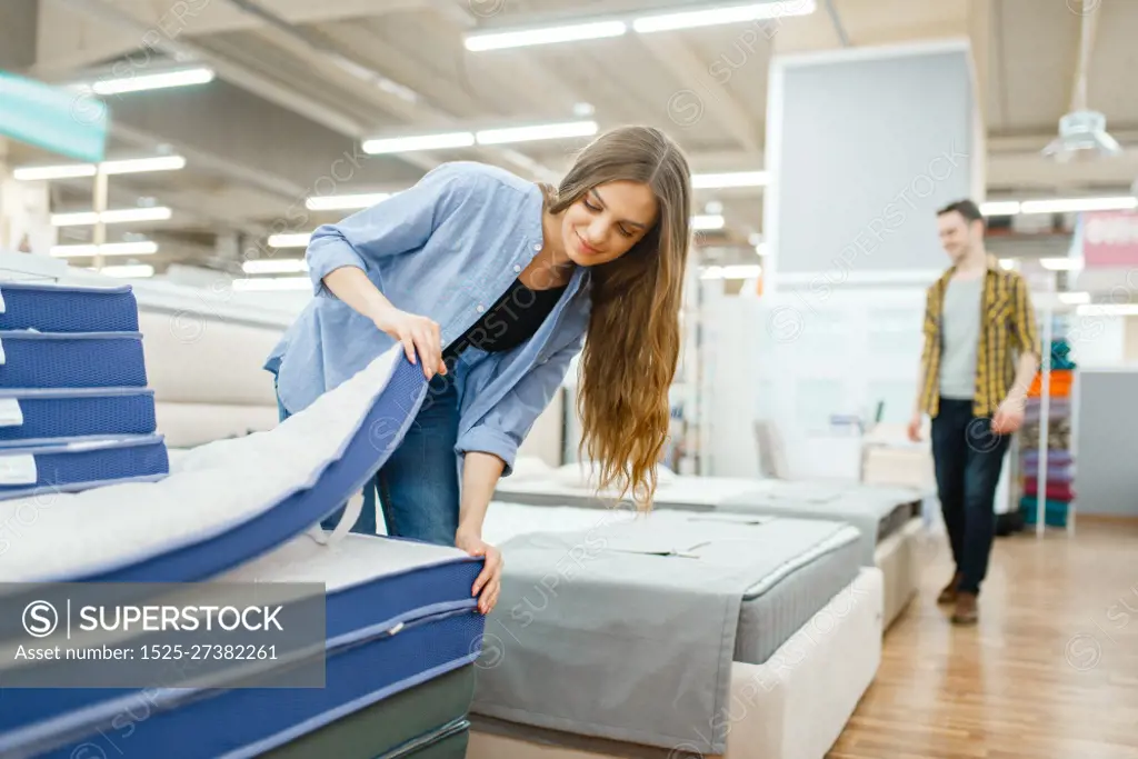 Young smiling couple in furniture store showroom. Man and woman looking samples for bedroom in shop, husband and wife buys goods for modern home interior. Young smiling couple in furniture store showroom