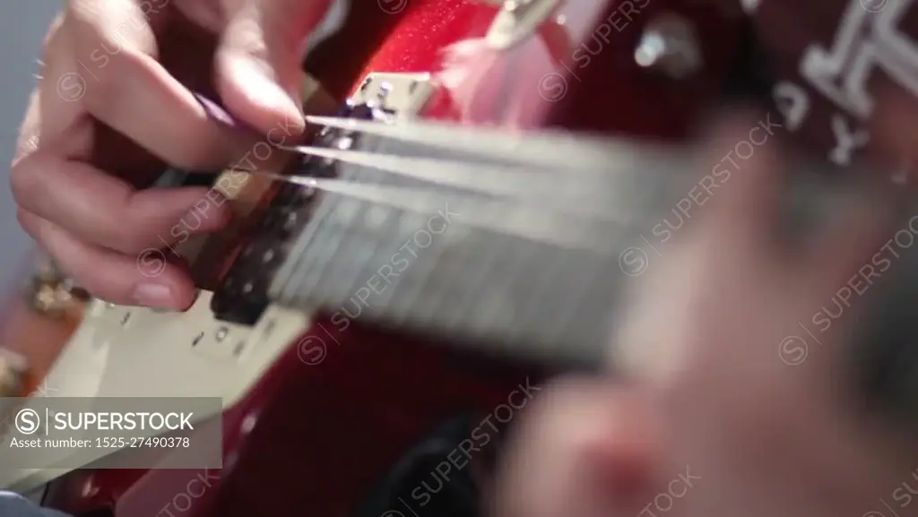 Close up of rock musician hand strumming at electric guitar strings. Man playing electric guitar with different techniques bending and tapping while recording a brand new song in studio. SuperStock