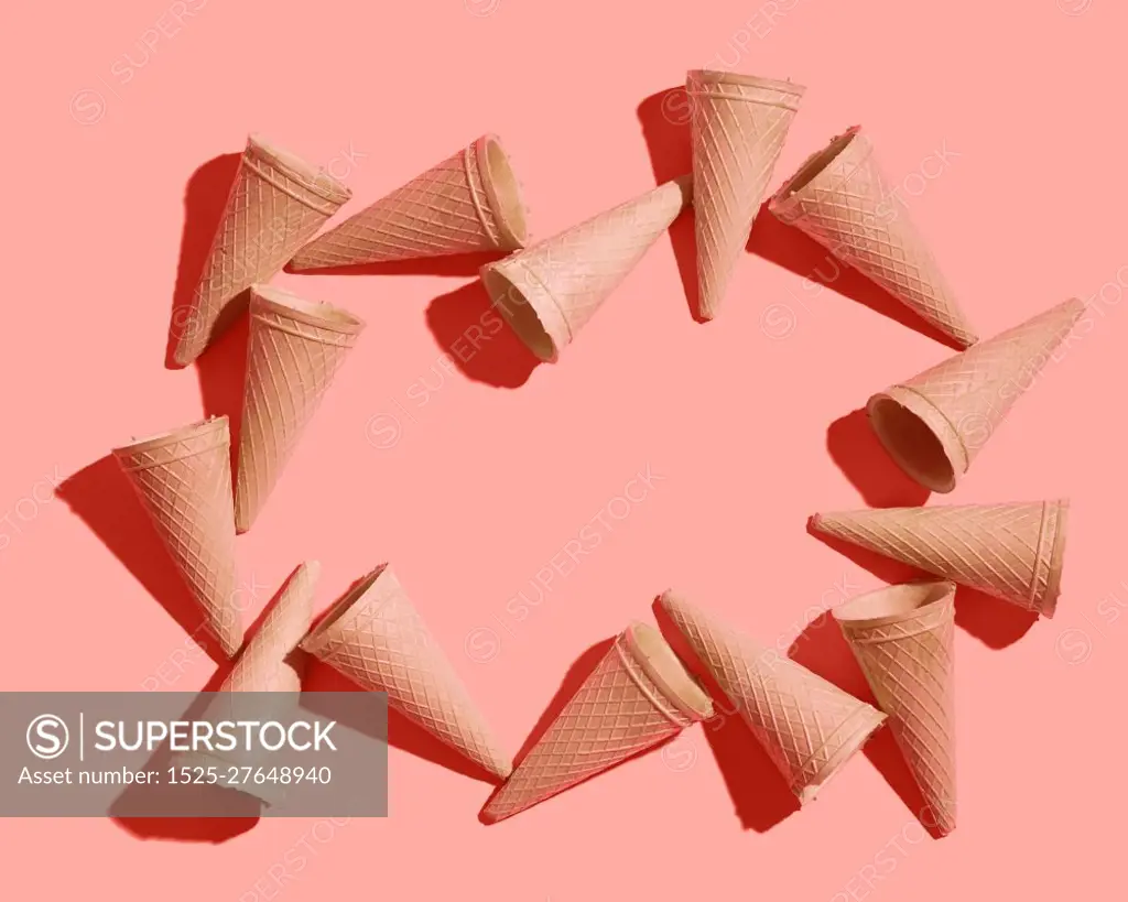 Frame from sweet wafer cones for dessert empty on a color background of the year 2019 Living Coral Pantone, place for your text. Spring or summer food concept. Top view.. Waffle sweet cones pattern on a color background of the year 2019 Living Coral Pantone. Place for text. Flat lay.