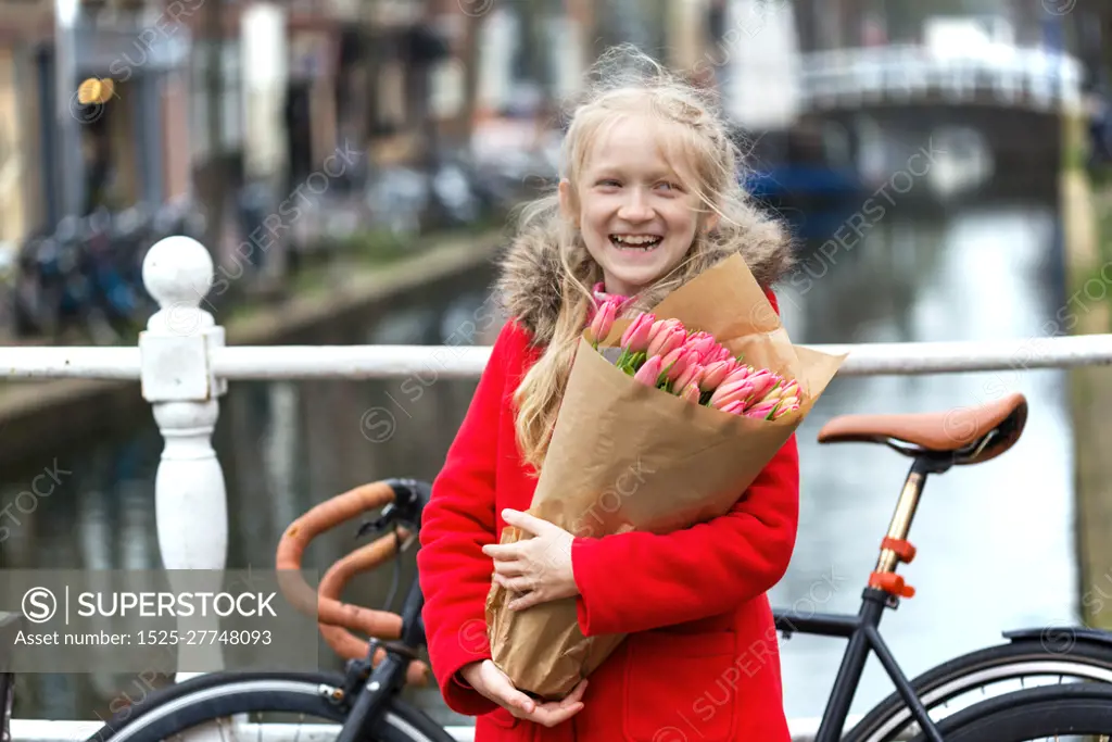 happy girl holding a bouquet of tulips sitting on a bench on a street of Amsterdam. The Netherlands