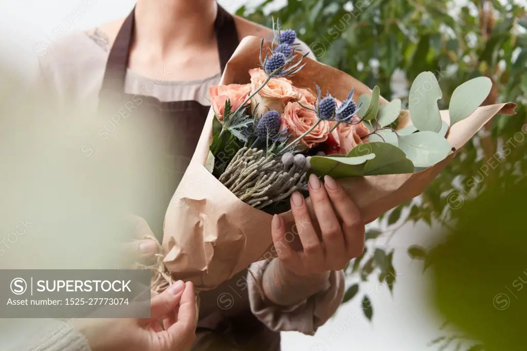 Bouquet of fresh fragrant roses living coral color in a paper with blured green leaf background. Concept of Mother Day.. Close-up of roses flowers bouquet in a woman&rsquo;s hands on a blured green leaf background.