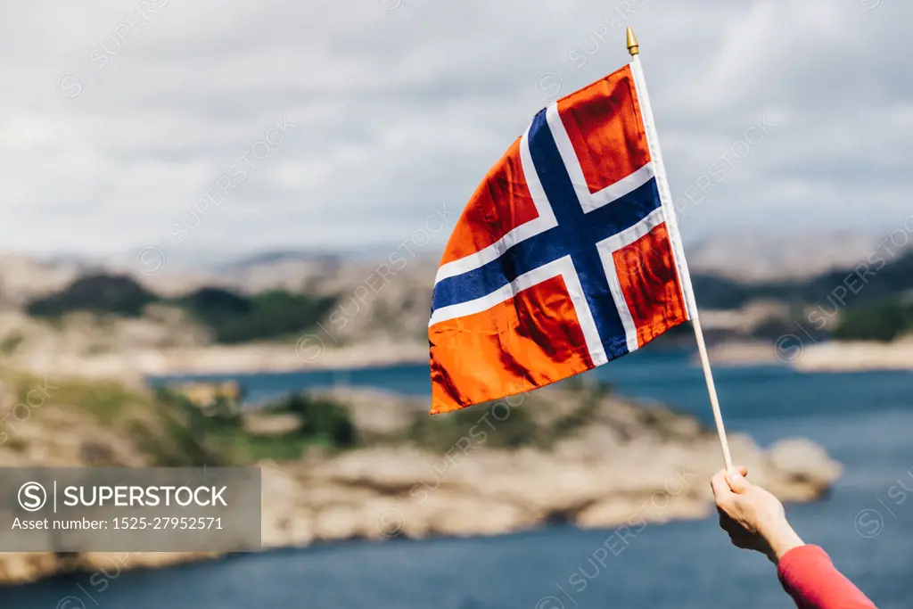 Tourist hand holding norwegian flag on rocky stone sea coast background.. Tourist with norwegian flag on sea coast