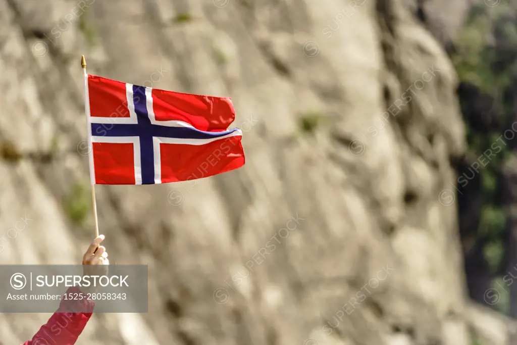 Tourist hand holding norwegian flag on rocky stone mountains background.. Tourist with norwegian flag in rocks mountains