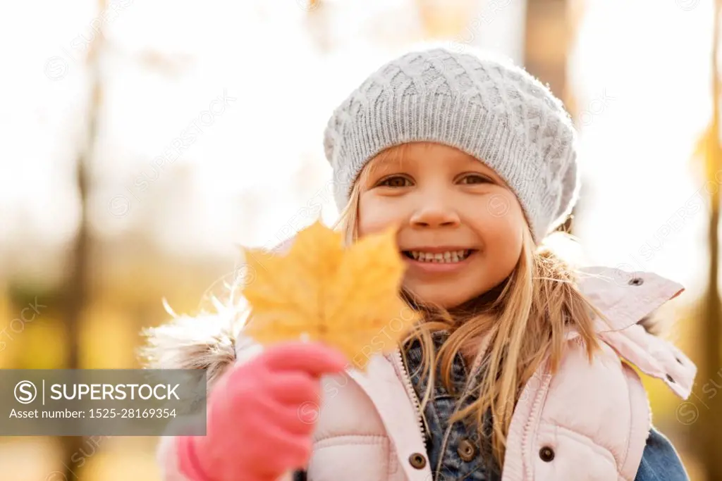 childhood, season and people concept - happy little girl with maple leaf at autumn park. happy little girl with maple leaf at autumn park