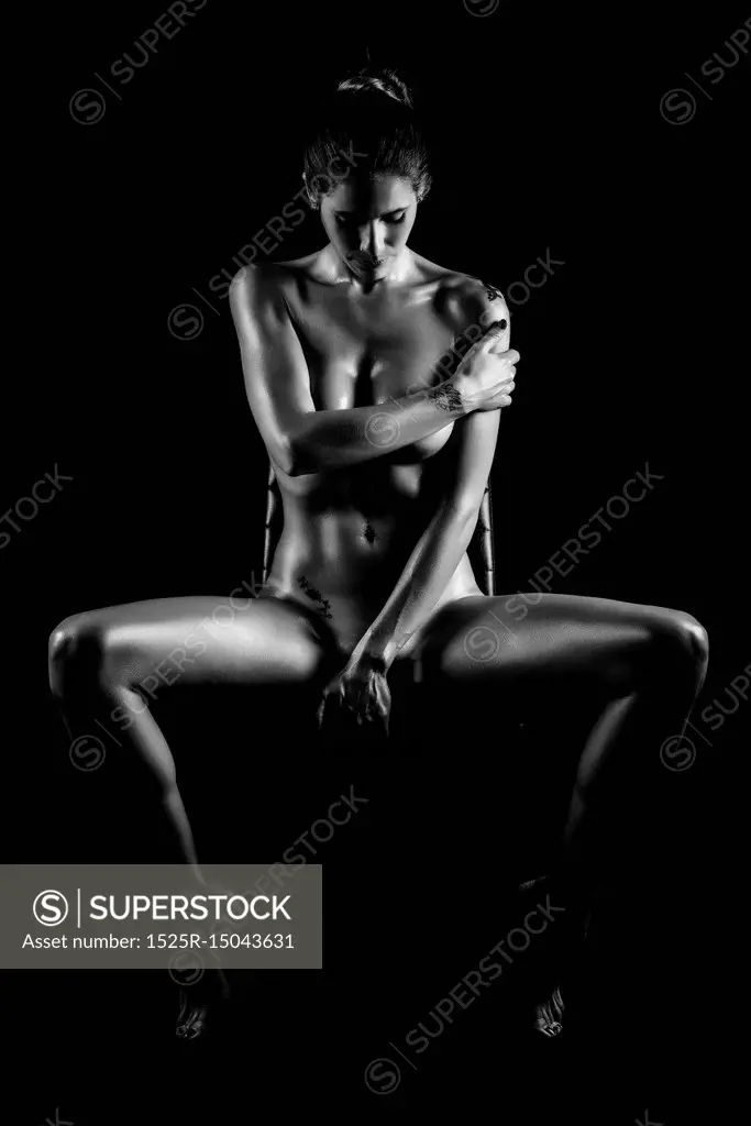 Young naked woman posing on black background. Perfect skin. Black and white photograph