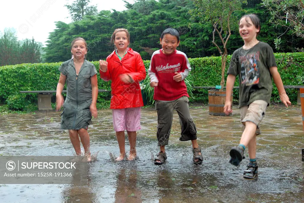 Four children jumping in rain and puddle