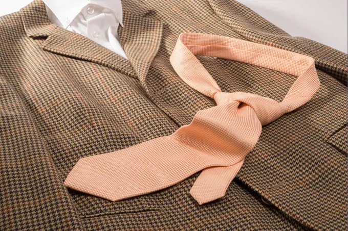 An orange and white dotted tie , already in a knot, lies on a brown sports jacket together with a white color shirt.