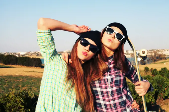 Two teen girl friends having fun together with skate board. Outdoors, urban lifestyle.