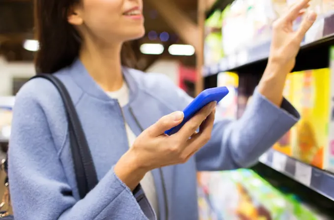 sale, shopping, consumerism and people concept - happy young woman with smartphone choosing and buying food in market