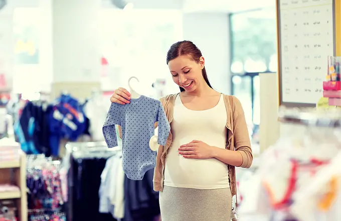 pregnancy, people, sale and expectation concept - happy pregnant woman shopping and buying baby bodysuit at children clothing store