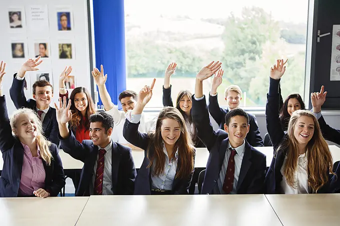 Teenage schoolchildren with hands raised in classroom