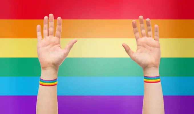 lgbt, same-sex relationships and homosexual concept - close up of male hands wearing gay pride awareness wristbands over rainbow colors background. hands with gay pride rainbow wristbands. hands with gay pride rainbow wristbands