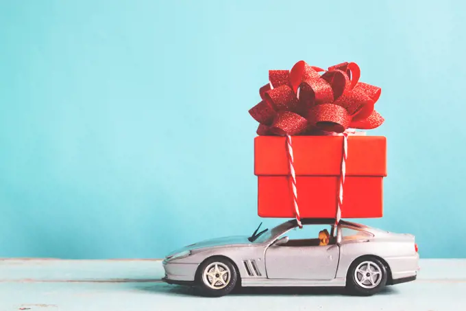 Red gift box on car toy with blue pastel color background, retro filter effect