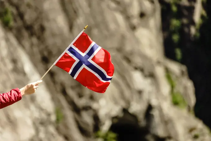 Tourist hand holding norwegian flag on rocky stone mountains background.. Tourist with norwegian flag in rocks mountains