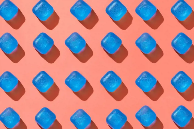 Blue plastic ice cubes pattern geometrical diagonal with hard shadows on a background in a color of the year 2019 Living Coral Pantone. Flat lay. Ceometrical pattern from blue plastic cubes with shadows on a background in a color of the year 2019 Living Coral Pantone. Top view.