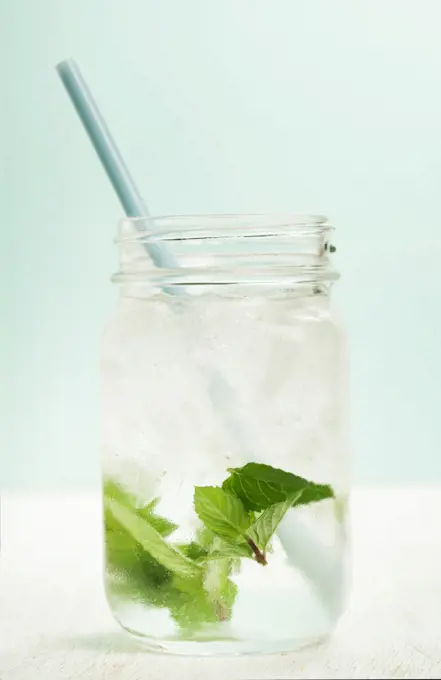 glass of cold water with fresh mint leaves and ice cubes on turquoise background